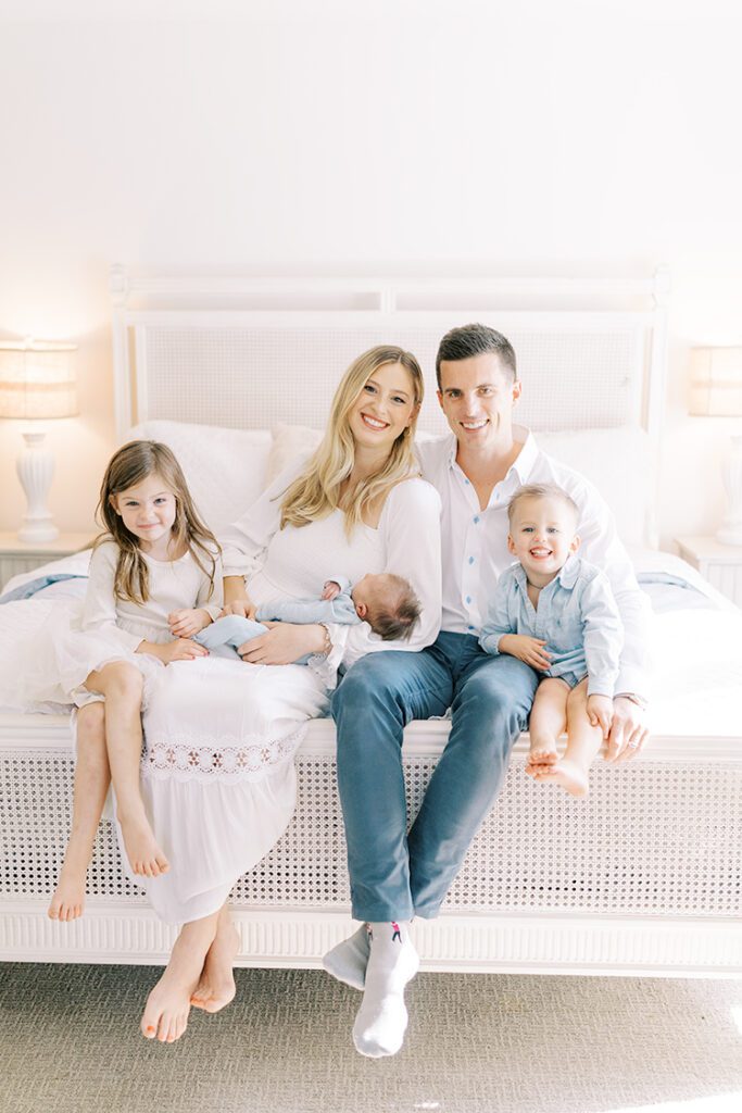 Family of five sitting on end of bed in  master bedroom, smiling at the camera at their photoshoot with family photographer in crestwood, ky